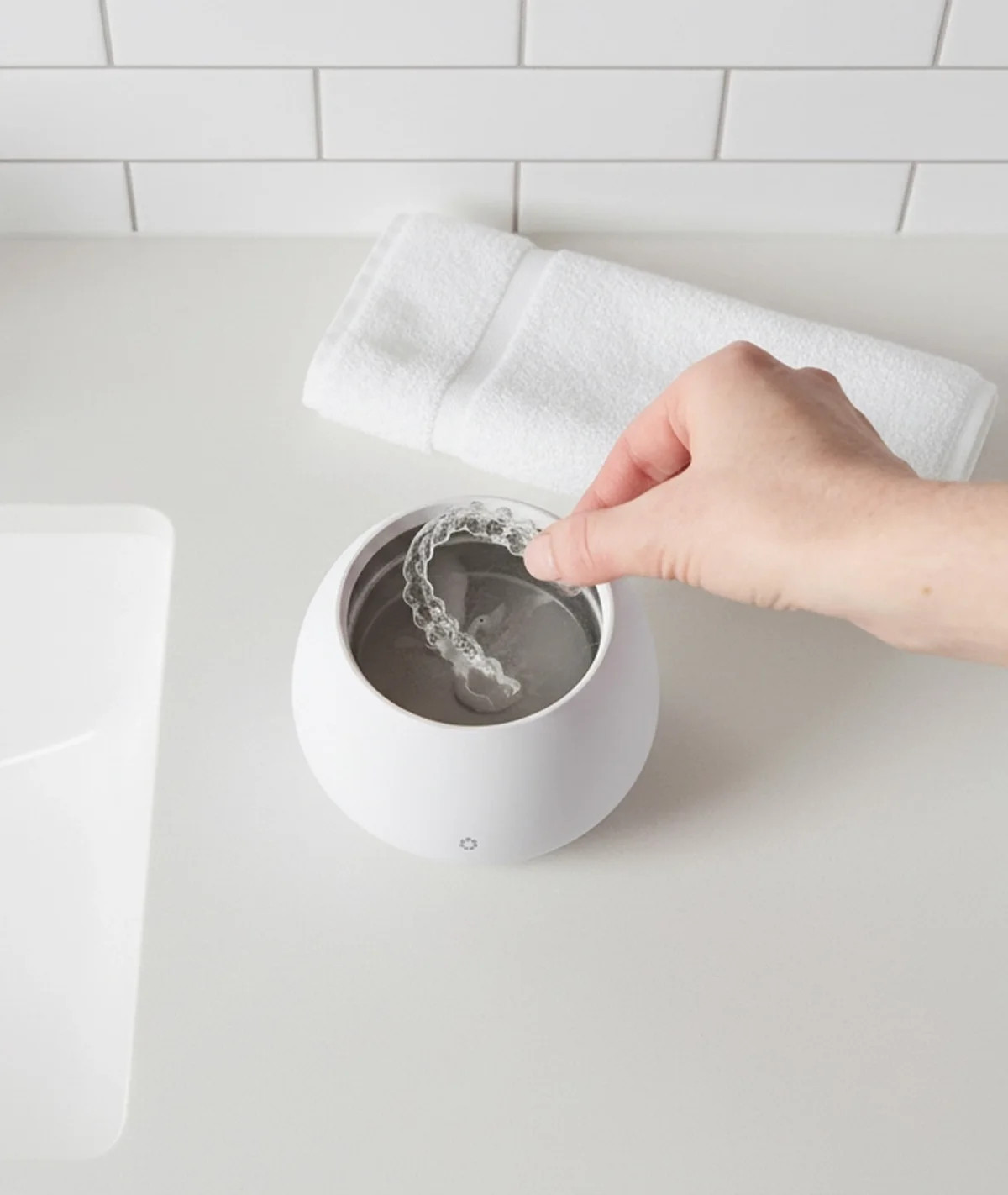 A hand lowering a clear dental tray into an open white Zima Dental Pod beside a bathroom sink.