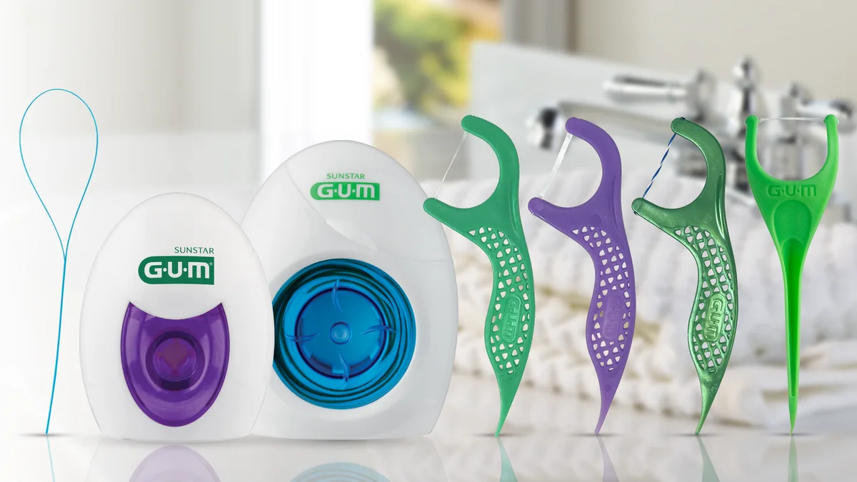 Two GUM dental floss dispensers, a floss threader and four handheld flossers beside a bathroom sink.