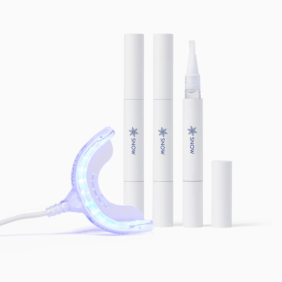 Three white SNOW whitening serum pens beside an illuminated wired mouthpiece on a white background.